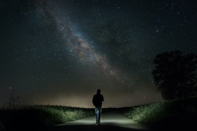 夜晚，在星空下绿草间的水泥路上行走的人